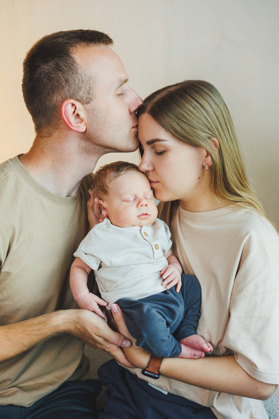 Yeni doğmuş bebeği olan mutlu bir aile. Güzel anne ve baba çocuklarını öpüyor. Anne baba ve gülümseyen çocuk, beyaz arka planda izole edilmiş.. - Fotoğraf, Görsel