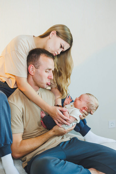 Yeni doğmuş bir bebeği olan genç bir aile. Mutlu anne ve baba çocuklarını öpüyor. Ebeveynler ve kollarında gülümseyen bir çocuk. - Fotoğraf, Görsel