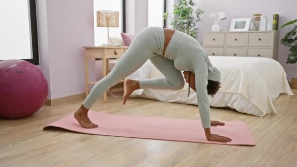 A woman in activewear practices yoga on a pink mat in a bright indoor bedroom with a exercise ball - Footage, Video