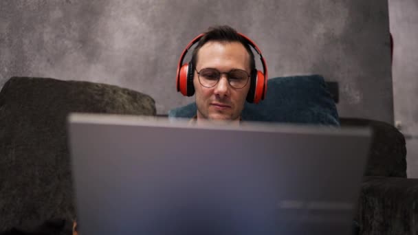 Relaks poważne kaukaski facet student freelancer za pomocą laptopa urządzenia opierającego się na kanapie w biurze domu, skupiony przedsiębiorca pracuje na odległość wpisując na notebooku w mieszkaniu - Materiał filmowy, wideo