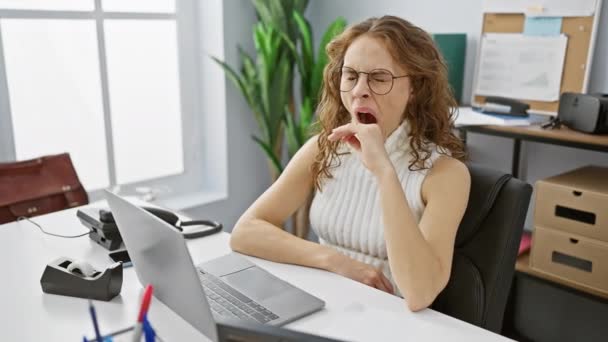 Mujer joven con exceso de trabajo, aburrida y bostezando en la oficina, luchando contra la somnolencia con la mano sobre la boca - Imágenes, Vídeo