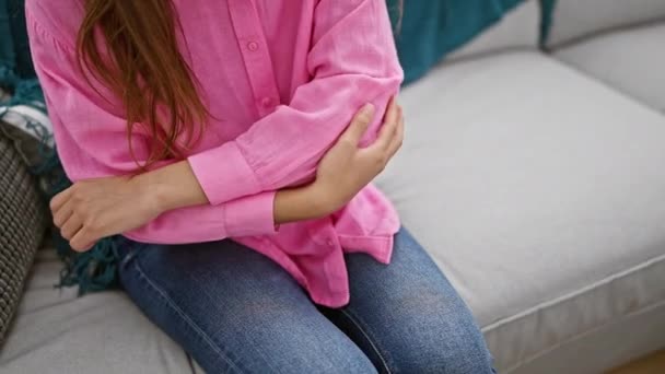 Schöne junge hispanische Frau, die sich auf ihrem gemütlichen Wohnzimmersofa ausruht, besorgt schaut, während sie drinnen unter starken Ellbogenschmerzen leidet. - Filmmaterial, Video