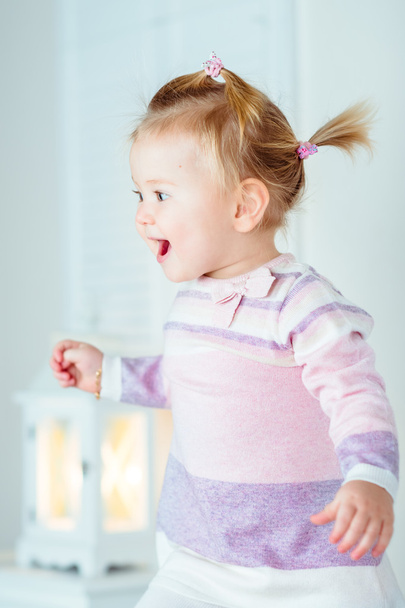 Excited blond little girl with ponytail jumping on bed, laughing and screaming. White interior, bedroom, night lamp - Photo, image