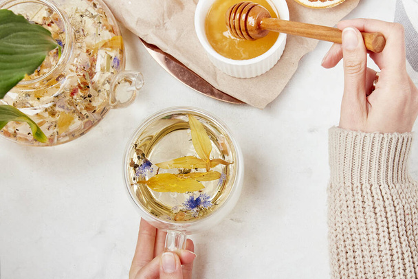 Woman hands add honey to tea cup. Healthy mountain herbal tea lifestyle. Detoxifying herbs concept - Photo, Image
