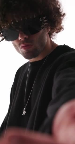 vídeo vertical de homem de moda legal com capuz preto com óculos de sol cravados convidando, sendo legal e fazendo um gesto de dedo de advertência no fundo cinza - Filmagem, Vídeo