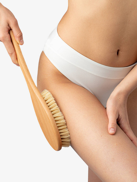 Donna strofinando la coscia con una spazzola da massaggio a secco - Foto, immagini