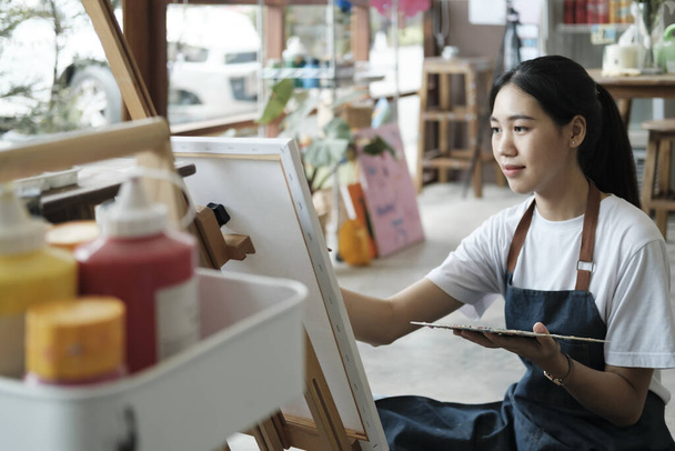 Jonge vrouwelijke kunstenares schetst of schildert haar tekening op doek in een atelier. Een tienermeisje dat houdt van kunst en tekenen neemt de tijd om haar aquarellen op doek te maken met grote intentie - Foto, afbeelding