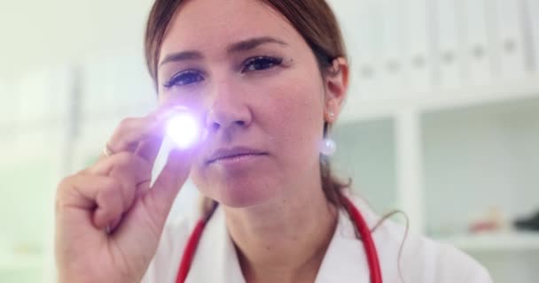 Doctor looks with stethoscope and shines flashlight into camera. Neurologist or ophthalmologist eye examination - Footage, Video