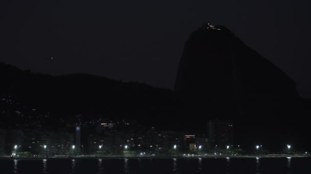 Atemberaubendes Nachtvideo mit dem berühmten Copacabana-Strand, dem majestätischen Zuckerhut und einem Flugzeug unter den Sternen. - Filmmaterial, Video
