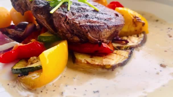 Grilled steak with a side of roasted potatoes and a colourful selection of grilled vegetables, drizzled with a peppercorn sauce - Footage, Video
