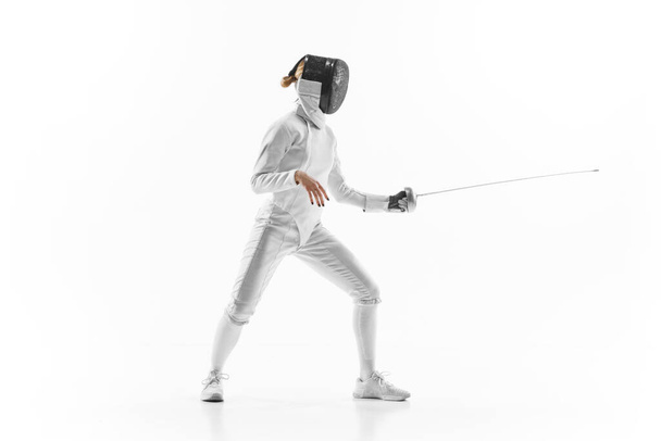 Female athlete in fencing gear showcasing her impeccable form, sword poised for action against white studio background. Confidence and strength. Concept of professional sport, active lifestyle. Ad - Photo, Image