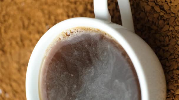 Hete instant koffie in een kopje tegen de achtergrond van koffie granules, bubbels barsten op het oppervlak van de drank, stoom komt eraan - Video