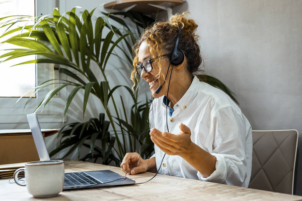 Mulher encaracolada com óculos usando laptop, comunicando na Internet com o cliente em casa, escritório de trabalho acolhedor, trabalho remoto, conceito de e-learning - Foto, Imagem