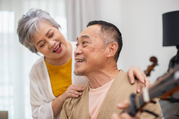 Mutlu Asyalı yaşlı çift emeklilik tatillerinde evde gitar çalarak eğleniyor, birlikte şarkı söylüyor. Yaşlandıkça birbirlerine bakıyorlar.. - Fotoğraf, Görsel