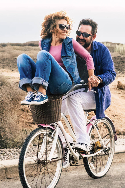 Joyful love friendship concept - happy adult caucasian, couple having fun with bicycle in outdoor leisure activity. concept of active playful people with bike during vacation - everyday joy lifestyle without age limitation - Photo, Image