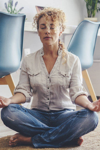 Gesunde Zen-Frauen machen Yoga und Meditation zu Hause auf dem Teppichboden - erwachsene Frau und psychische Gesundheit oder positive Freizeitaktivität im Lebensstil - schöne Dame sitzt mit geschlossenen Augen und ausgewogener Lotus-Haltung - Foto, Bild