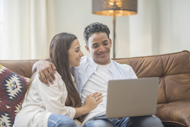 Genç çift yeni bir ev bilgisayar laptop kullanarak kanepede oturan rahatlatıcı, yeni daireye taşımak için mutlu gülümseyen hareket - Fotoğraf, Görsel
