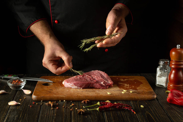Додавання розмарину до м'яса руками шеф-кухаря для аромату та смаку. Процес приготування яловичого стейка на кухонному столі зі спеціями та перцем - Фото, зображення