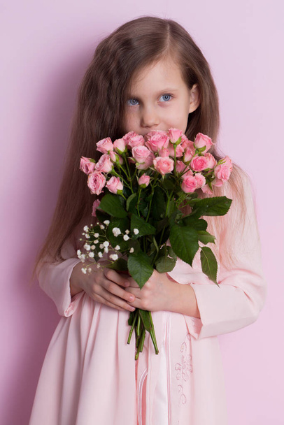 Egy csinos kislány rózsaszín ruhában rózsaszín rózsacsokrot tart rózsaszín háttéren. - Fotó, kép