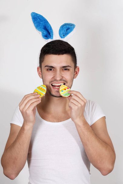 Joven guapo con una camiseta blanca y orejas de conejo sobre un fondo blanco. Concepto Pascua - Foto, Imagen