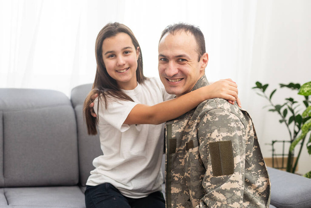 Klein meisje omhelst haar militaire vader thuis, close-up. Hoge kwaliteit foto - Foto, afbeelding