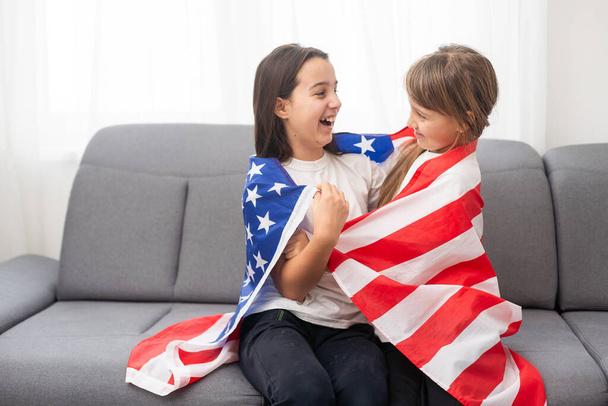 Χαρούμενα αξιολάτρευτα παιδιά που στέκονται κάτω από αμερικανική σημαία και κοιτάζουν. Υψηλής ποιότητας φωτογραφία - Φωτογραφία, εικόνα