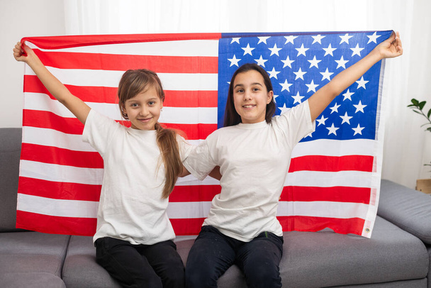 Brunette et blonde copines adolescentes en t-shirts blancs tenant drapeau américain, amis adolescents énergiques passer du temps, amitié. Photo de haute qualité - Photo, image