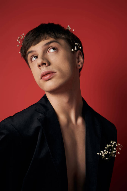 good looking young man in velvet blazer with flowers in hair looking at camera on red background - Photo, Image