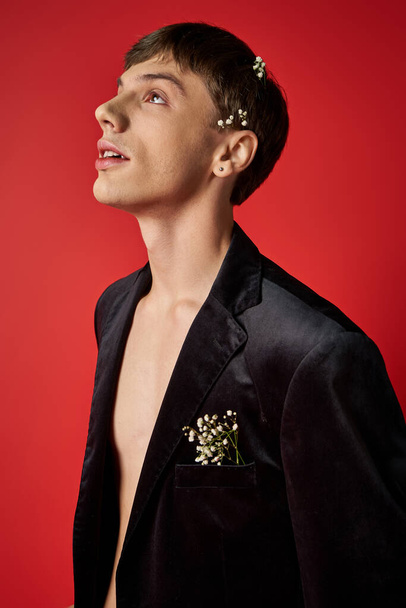 dreamy young male model in velvet blazer with flowers in hair looking up on red background - Photo, Image