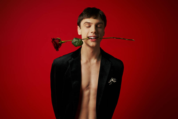 jóképű fiatalember bársony kabát gazdaság rózsa fogak és mosolygós piros háttér, romantika - Fotó, kép