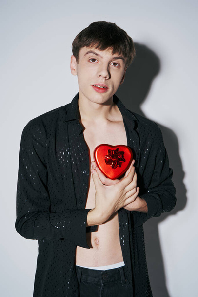 романтический молодой человек в рубашке с красным сердцем в форме настоящей коробки на сером фоне, День Святого Валентина - Фото, изображение