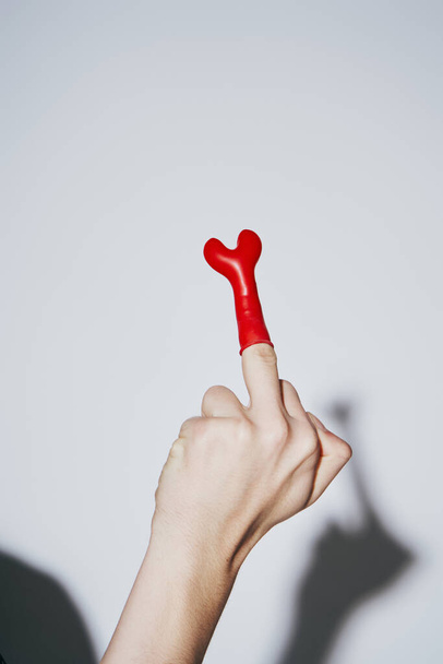 przycięty widok prowokacyjny młody człowiek pokazując środkowy palec z czerwonym balonem na szarym tle - Zdjęcie, obraz