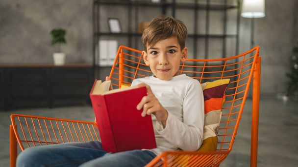 Un garçon enfant caucasien de sept ans enfant dans la chambre à la maison lire le livre - Photo, image