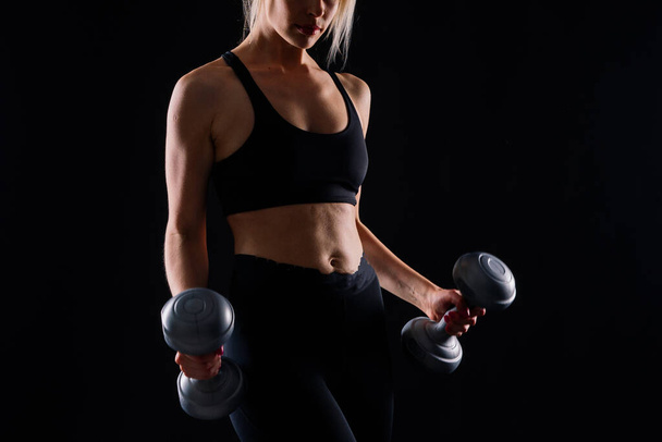 Athletic woman in a sportswear raises dumbbells leads healthy lifestyle has happy expression - Photo, Image
