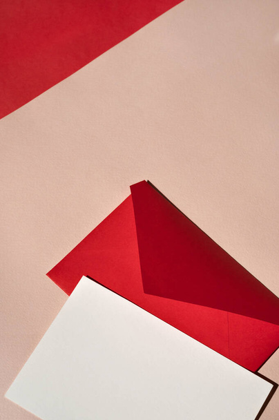 Czerwona koperta papierowa i makieta z pustą kartką na brzoskwiniowym beżowym tle, luksusowe święto estetyczne biznesowe markowe szablon, przestrzeń do kopiowania. - Zdjęcie, obraz