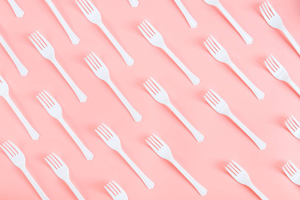 白いプラスチック製のフォークの多くは、薄いピンクの背景に斜めに、フラットを閉じるまで横たわっている。エコロジー、プラスチックごみ、使い捨てプラスチック食器の概念. - 写真・画像
