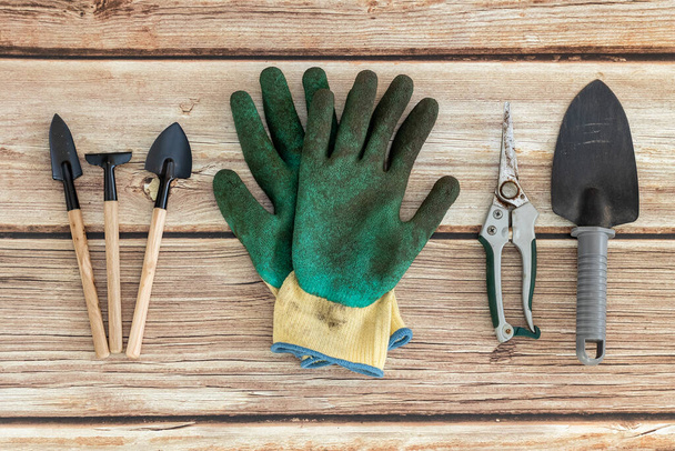 Des gants de jardinage sales et des outils à main de jardinage reposent sur une table en bois naturelle, à plat, en gros plan.. - Photo, image
