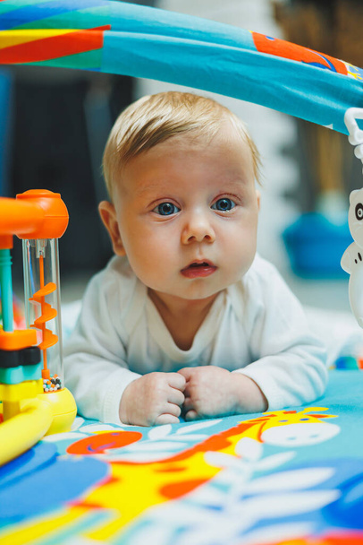 Un bebé juega en una estera de desarrollo durante dos meses. Alfombra de juguete para niños pequeños. - Foto, imagen