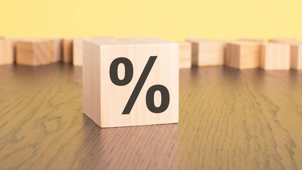 a wooden cube with a percentage sign rests on the brown table, against a yellow background. copy space - Photo, Image