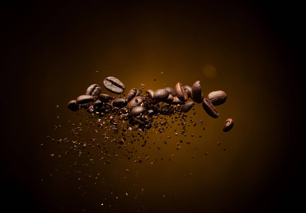 Καφές ψητά φασόλια εδάφους έκρηξη μύγα, καφέ θρυμματισμένο έδαφος επιπλέουν ρίχνει μείγμα με φασόλια. Ψητό κόκκους καφέ σκόνη έδαφος σκόνη βουτιά έκρηξη σκόνης στη μέση του αέρα. Μαύρο φόντο Απομονωμένο χρυσό bokeh - Φωτογραφία, εικόνα