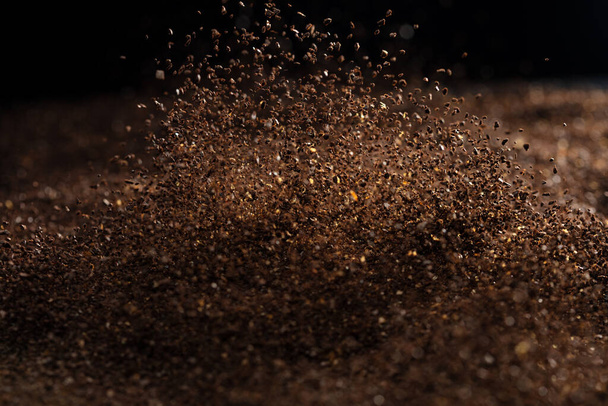 Ground Coffee roasted powder dust fly explosion, Coffee crushed ground float pouring. Roasted Coffee powder ground dust splash explosion in mid Air. Black background Isolated selective focus blur - Photo, image