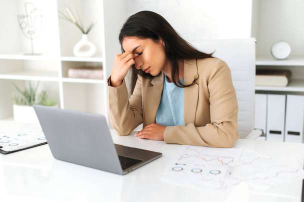 Розчарована перевтома арабська або індійська бізнес-леді, корпоративний юрист, менеджер, сидить на робочому місці, масажує носбрідж, відчуває головний біль, мігрень, стрес, потребує відпочинку - Фото, зображення