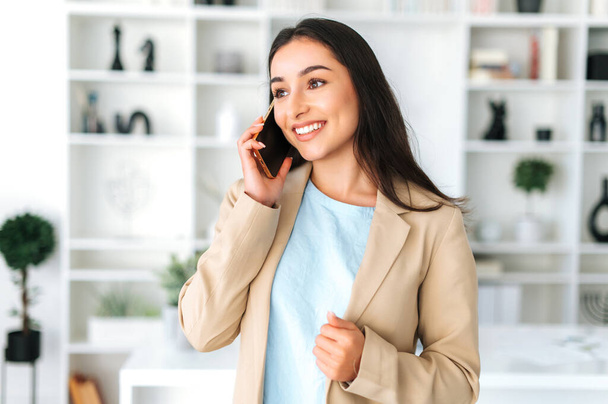 Телефонный разговор. Позитивная дружелюбная великолепная арабская или индийская женщина, руководитель компании, менеджер, беседующий по телефону с партнером или клиентом, обсуждающий вопросы работы, назначает встречу, улыбается - Фото, изображение