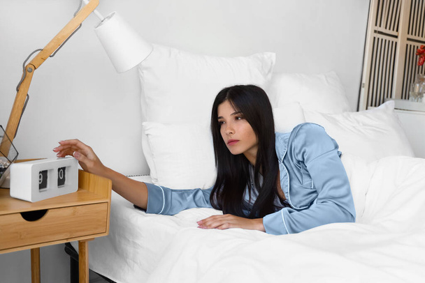 Fiatal nő kikapcsolja ébresztőóra az ágyban - Fotó, kép