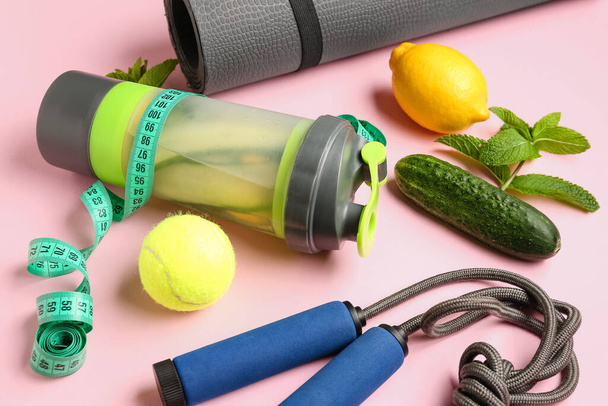 Пляшка лимонаду з огірком та спортивним обладнанням на рожевому фоні - Фото, зображення