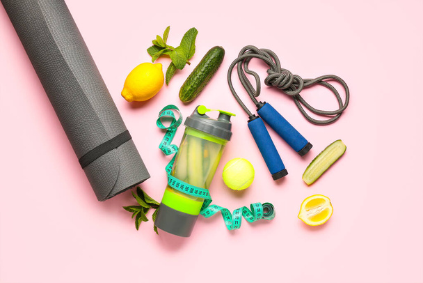 Bottle of lemonade with cucumber and sport equipment on pink background - Photo, Image