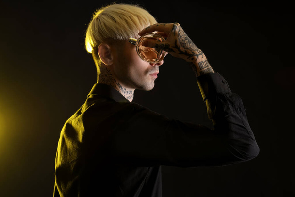 Tattooed young man with perfume on dark background, closeup - Photo, Image