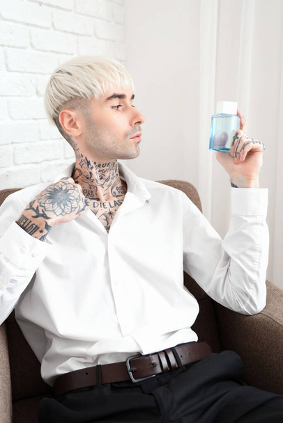 Tetovált fiatalember parfümmel otthon ül a karosszékben. - Fotó, kép