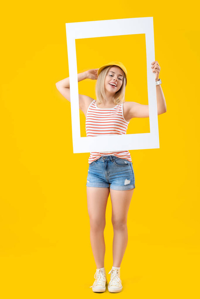 Young beautiful happy woman with frame on yellow background - Photo, Image