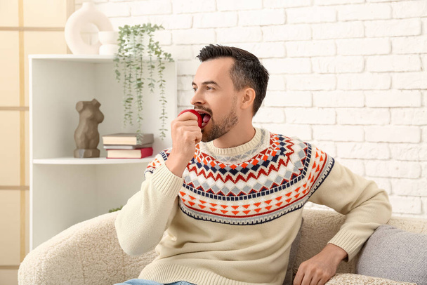 Όμορφος άνθρωπος τρώει μήλο στον καναπέ στο σπίτι - Φωτογραφία, εικόνα